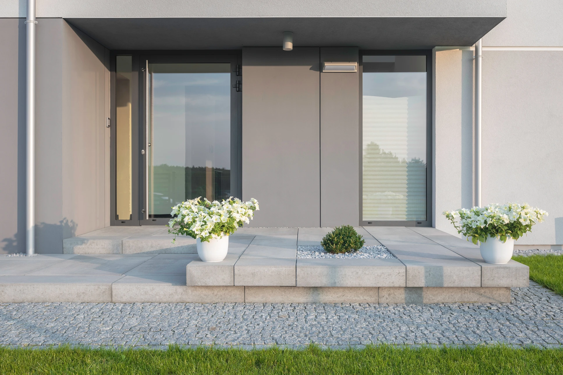 Entrée moderne d'une maison contemporaine avec escalier en béton et jardinières blanches fleuries