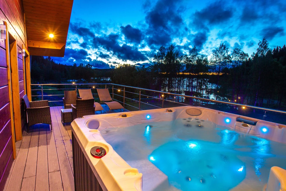Terrasse en bois avec spa jacuzzi illuminé en bleu, mobilier de jardin en rotin, balustrade métallique