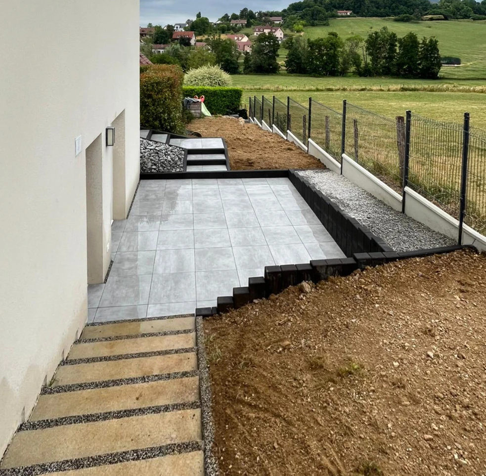 Aménagement paysager extérieur résidentiel avec escaliers en pierre naturelle multicolore, terrasse surélevée en dalles beiges et marches intermédiaires