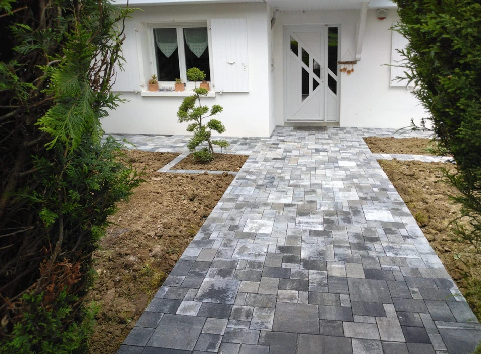 Terrasse extérieure aménagée avec salon de jardin modulaire en résine tressée, coussins gris et blancs, table basse ronde noire