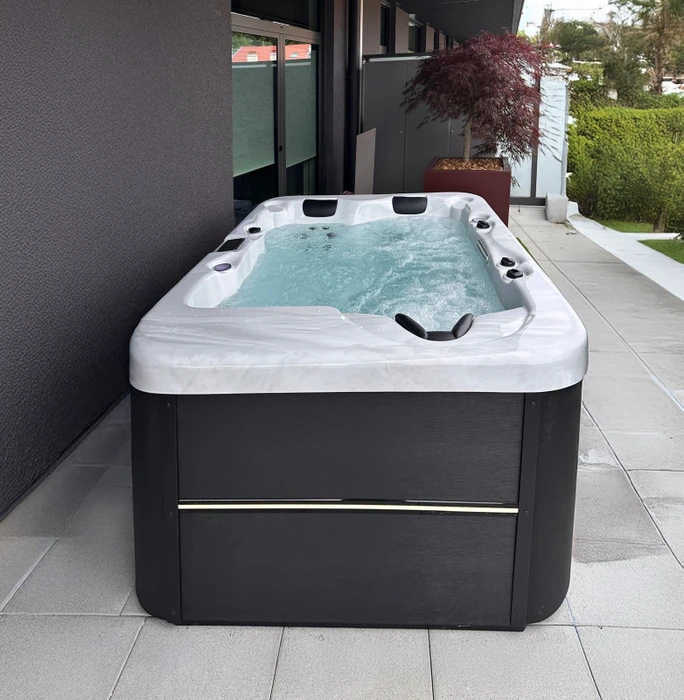 Terrasse extérieure d'un chalet en bois avec spa jacuzzi, paysage montagneux enneigé, coucher de soleil hivernal, arbres dénudés, balustrade en bois naturel