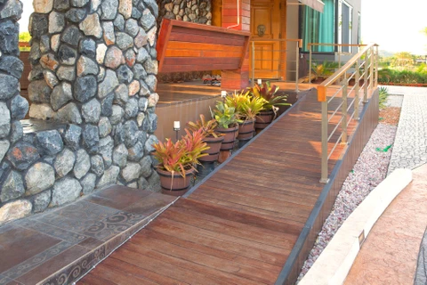 Entrée extérieure d'habitation moderne avec escalier en bois exotique, rampe métallique design et jardinières alignées contenant des plantes tropicales colorées