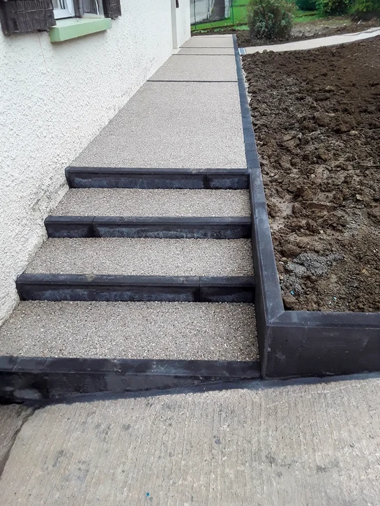 Escalier extérieur en pierre naturelle avec emmarchement élargi, menant à l'entrée d'un bâtiment blanc