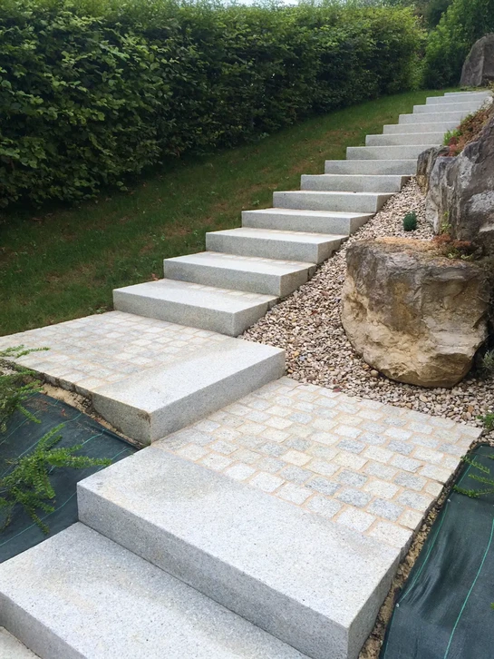 Entrée résidentielle avec escalier béton, rampe métallique décorative et porte d'entrée moderne